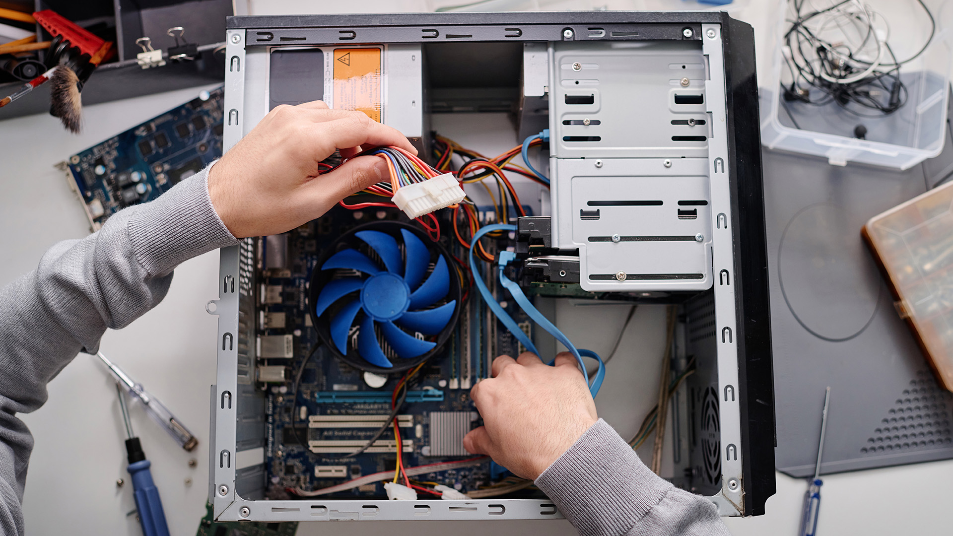 Hands connecting power supply cables to internal components inside a desktop PC case.