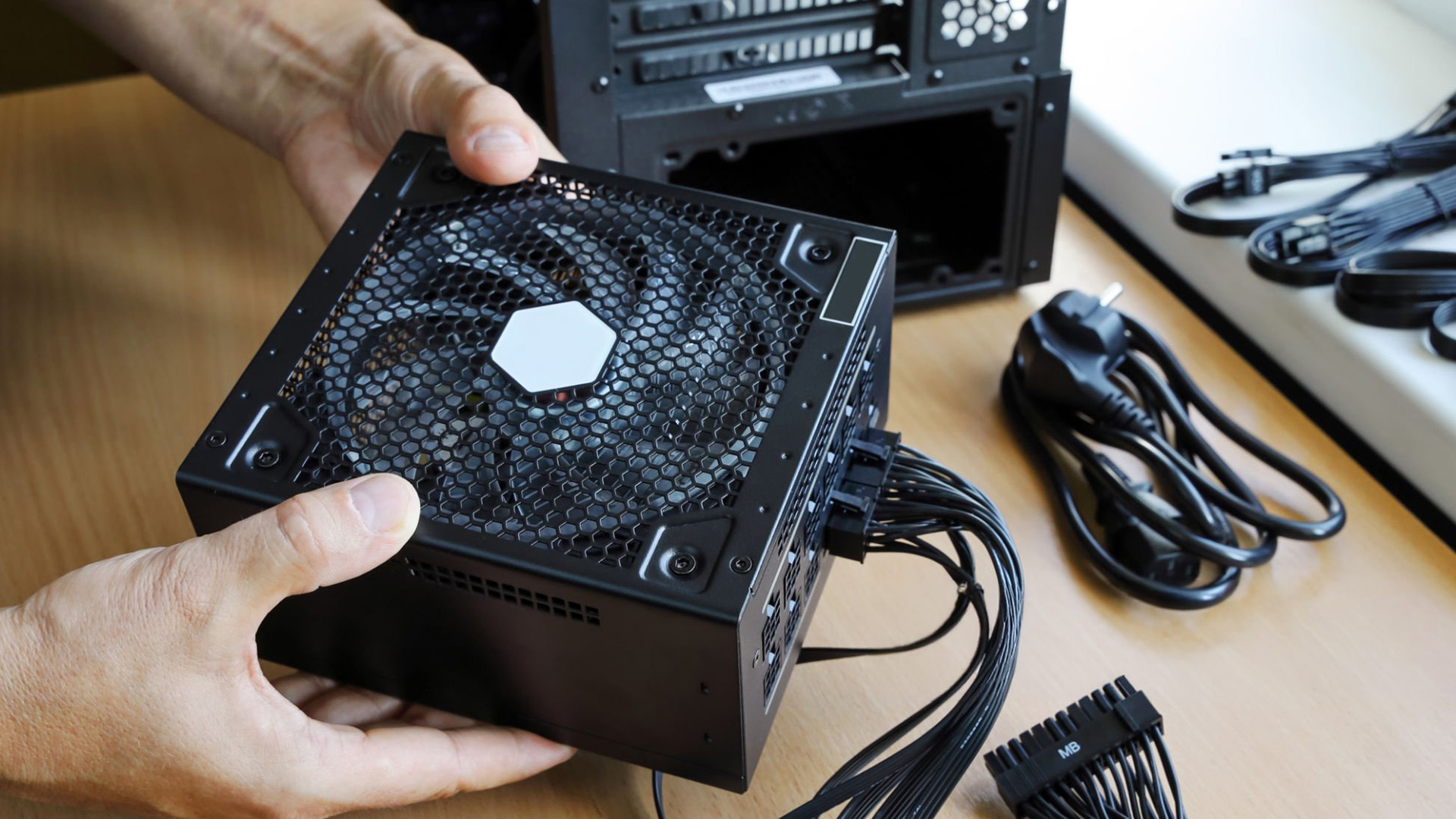 A person holding a modular power supply unit with connected black cables.