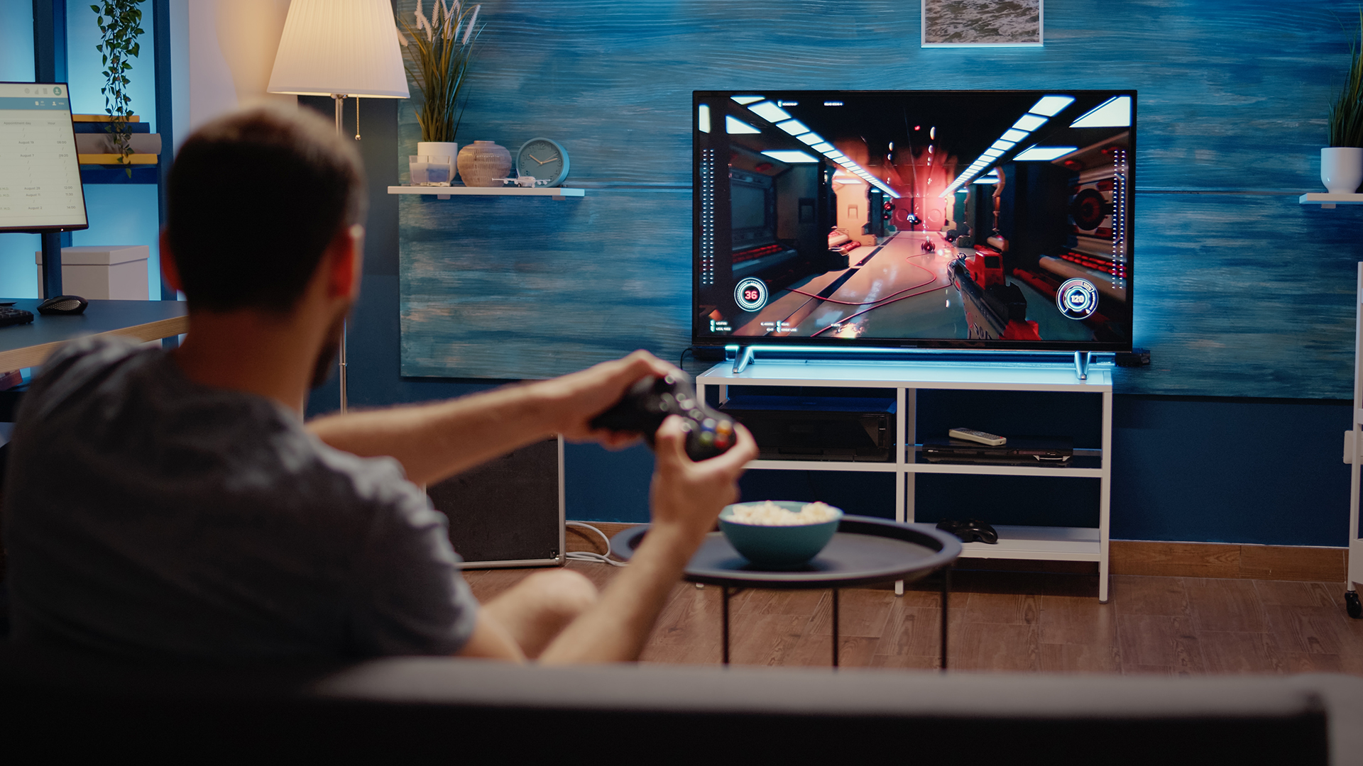 Person sitting in a living room playing a console game on a big screen TV.