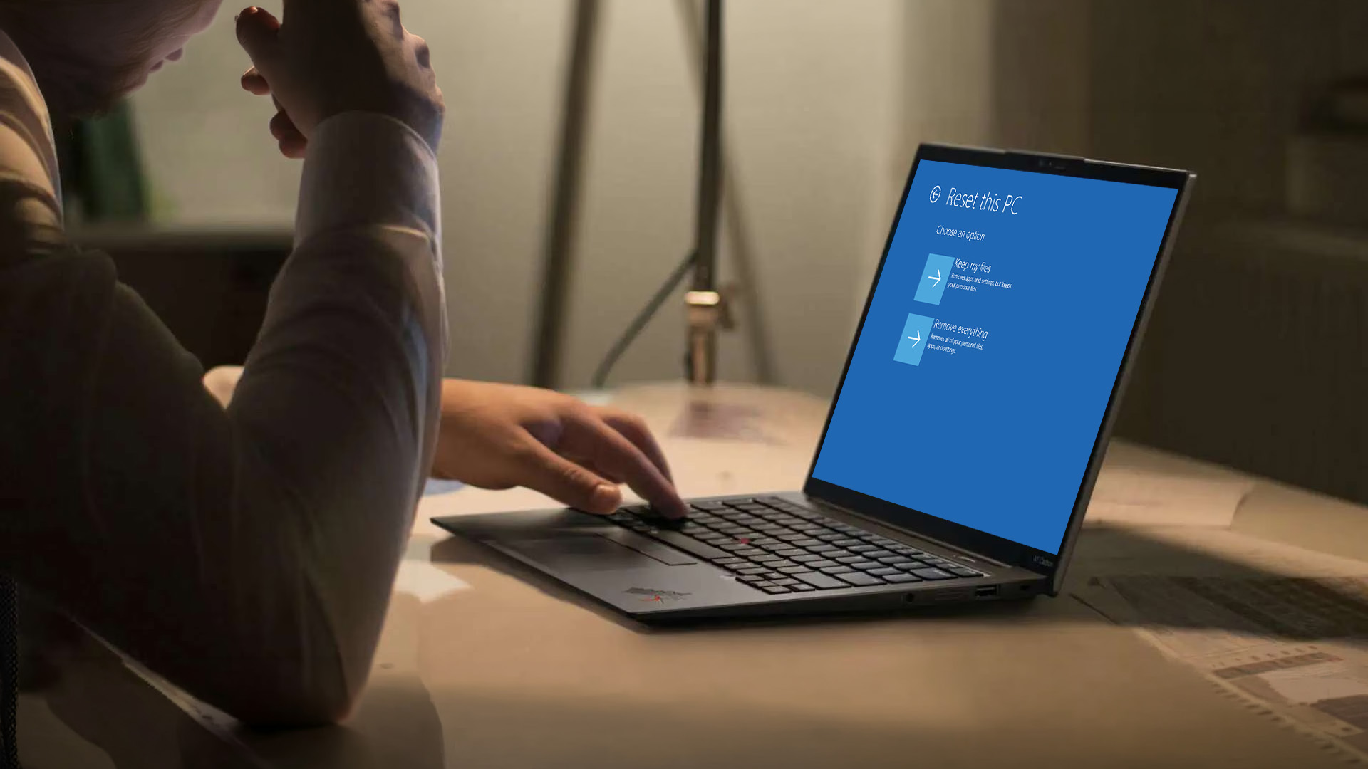 Person at a desk initiating a factory reset on a Lenovo ThinkPad laptop.