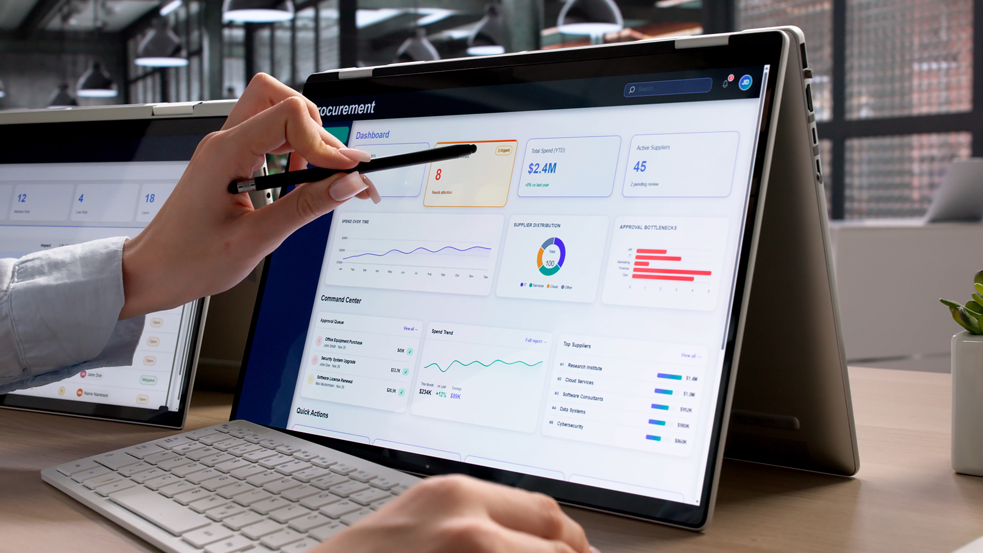 A person using a digital stylus on a detachable 2-in-1 laptop displaying data dashboards.