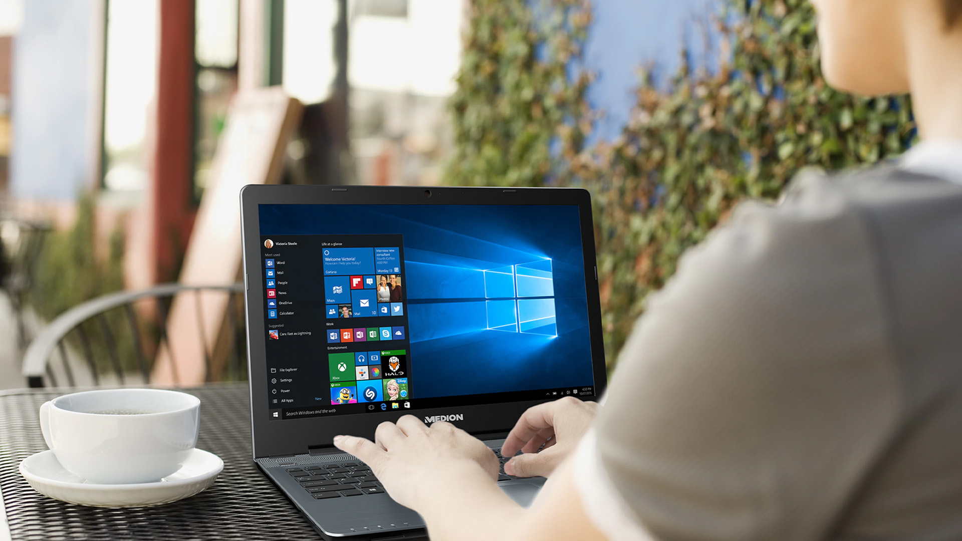 Person using a Medion laptop with Windows 10 at an outdoor cafe table.