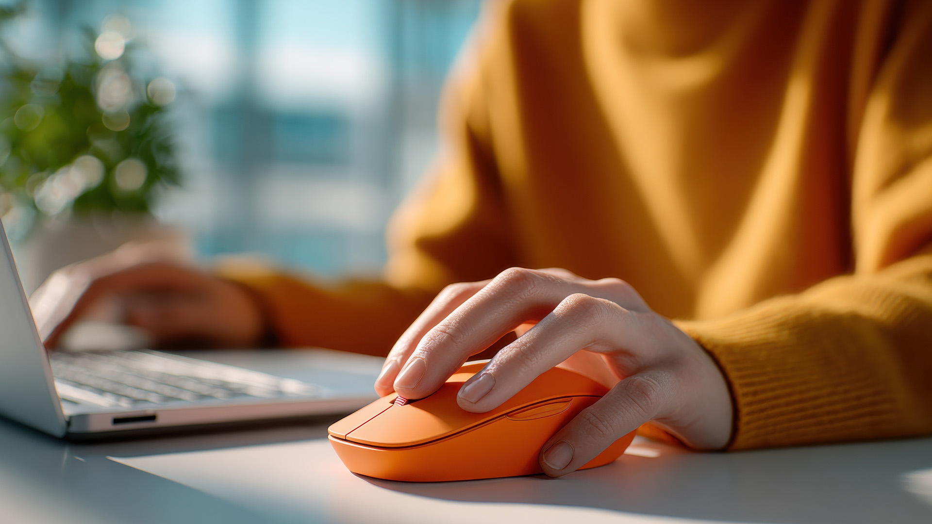 Person using an orange computer mouse with a laptop.