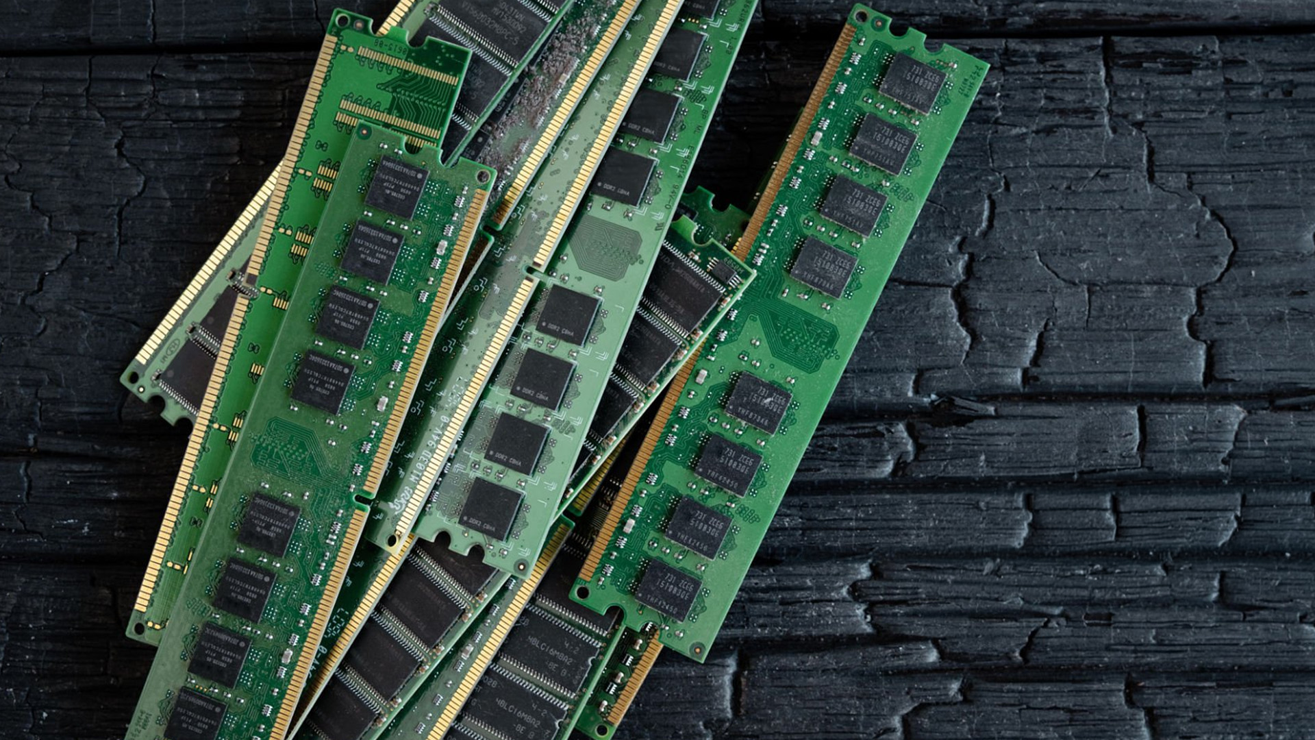 A pile of green computer RAM memory sticks resting on a dark textured wooden surface.