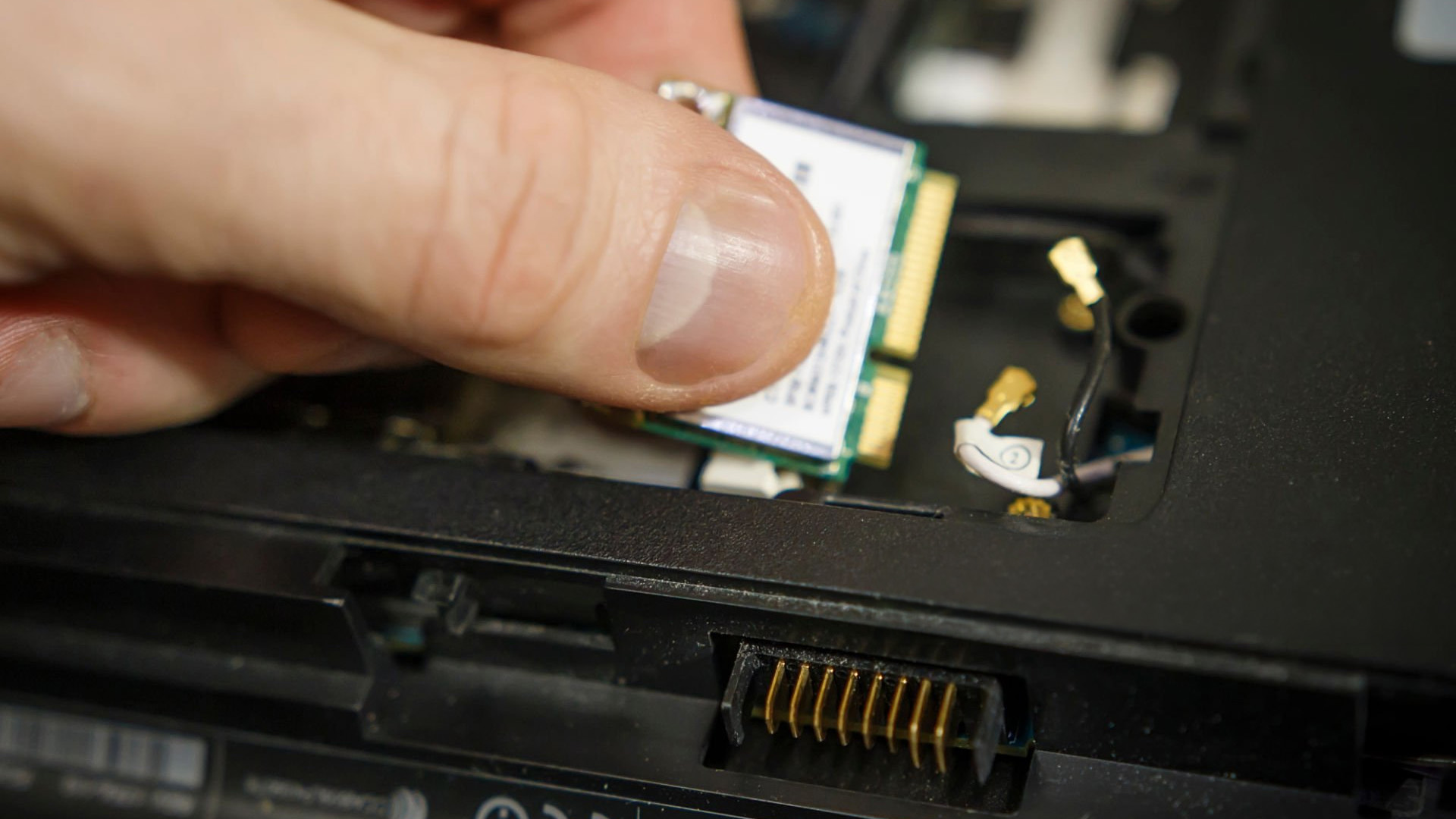 A person replacing a Wi-Fi card inside a laptop.