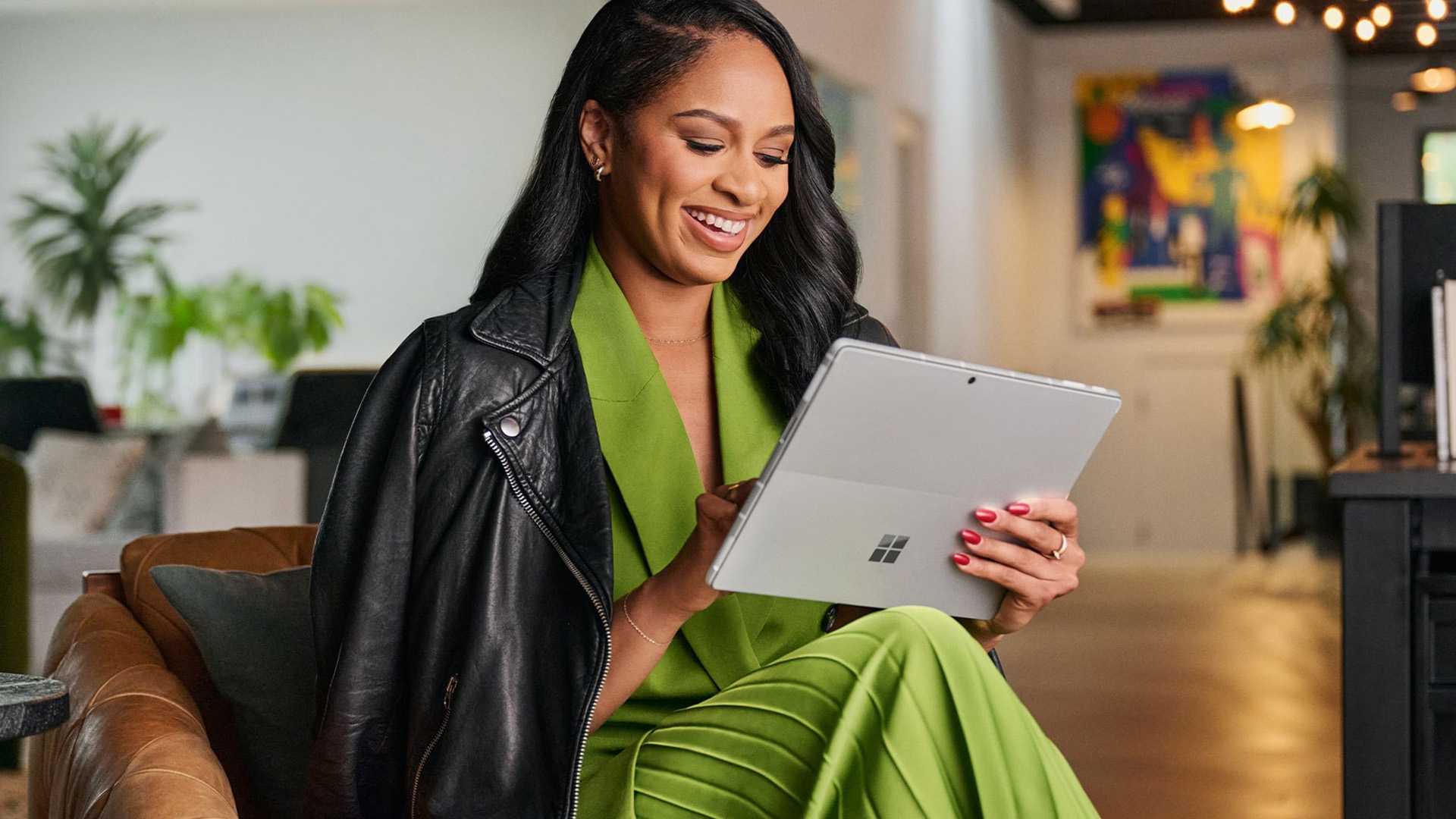 A smiling woman holding and using a Microsoft Surface Pro device in a bright modern office.