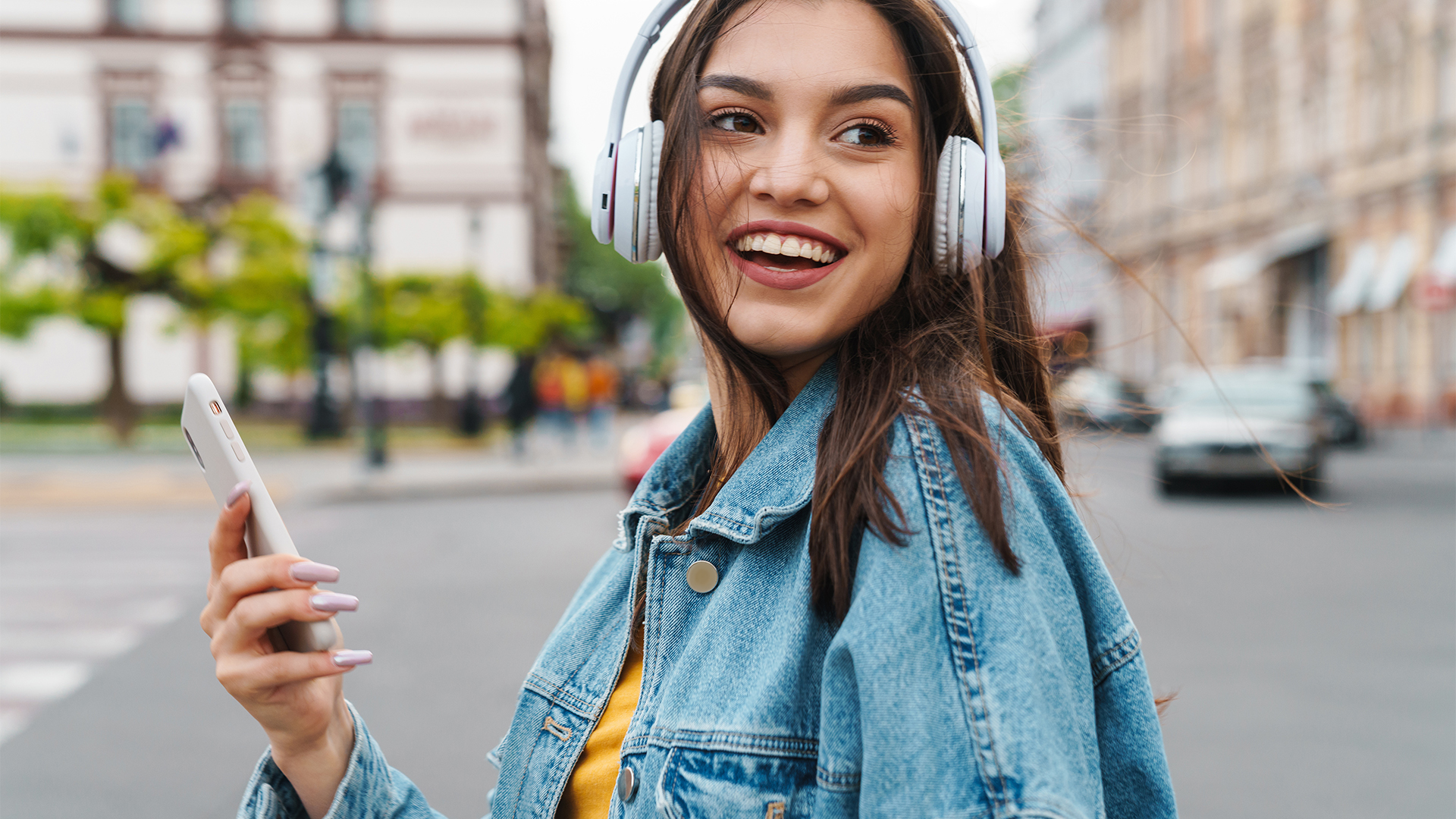 Smiling woman holding a smartphone and wearing wireless headphones.