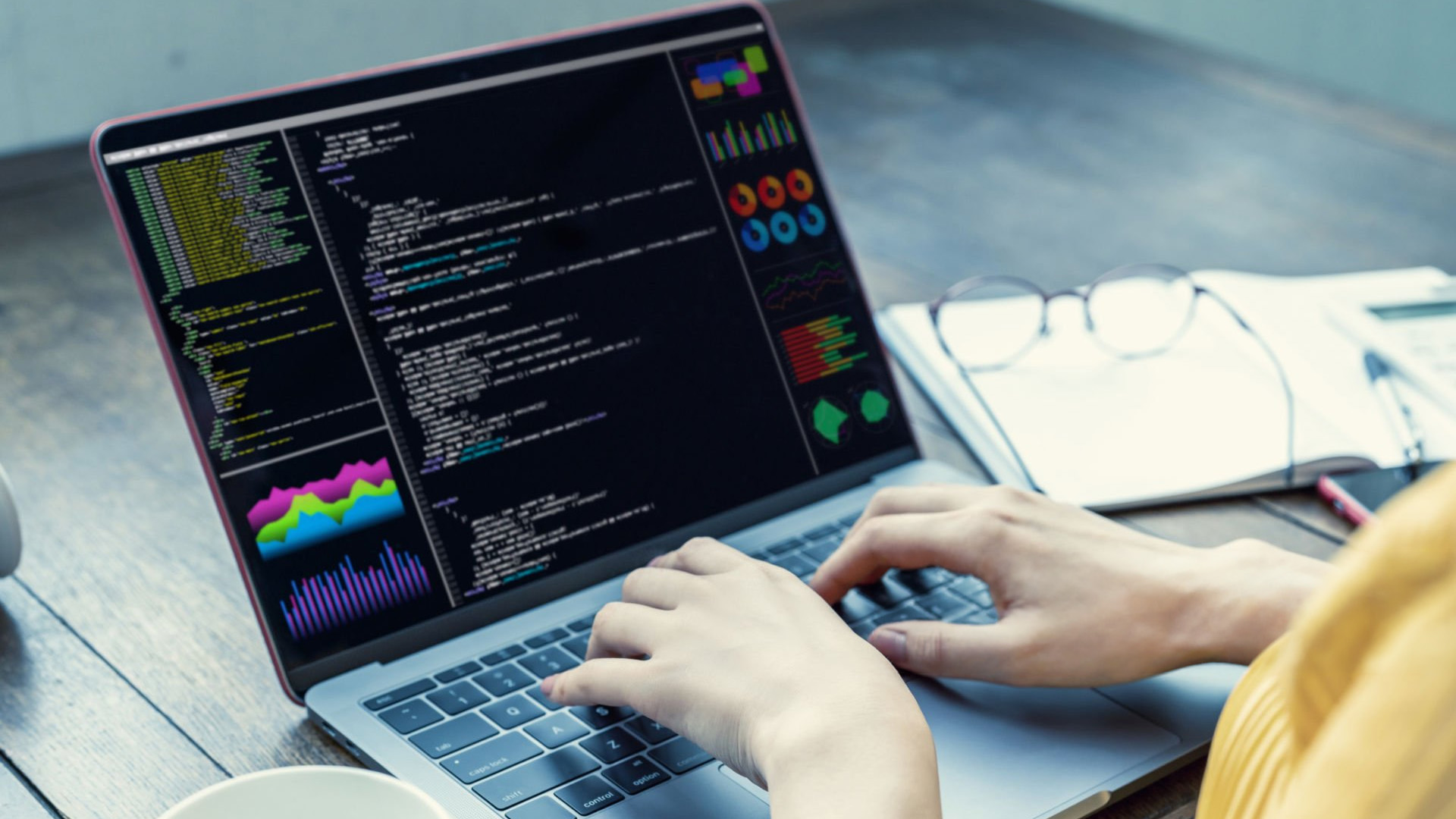 A software developer coding on a laptop screen showing code and data performance charts.
