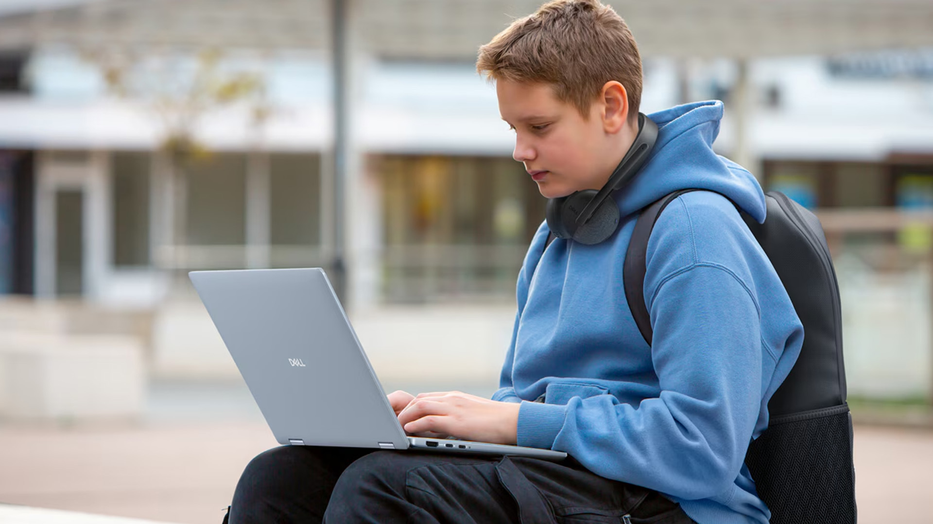 Young student wearing a hoodie and headphones typing on a Dell laptop.