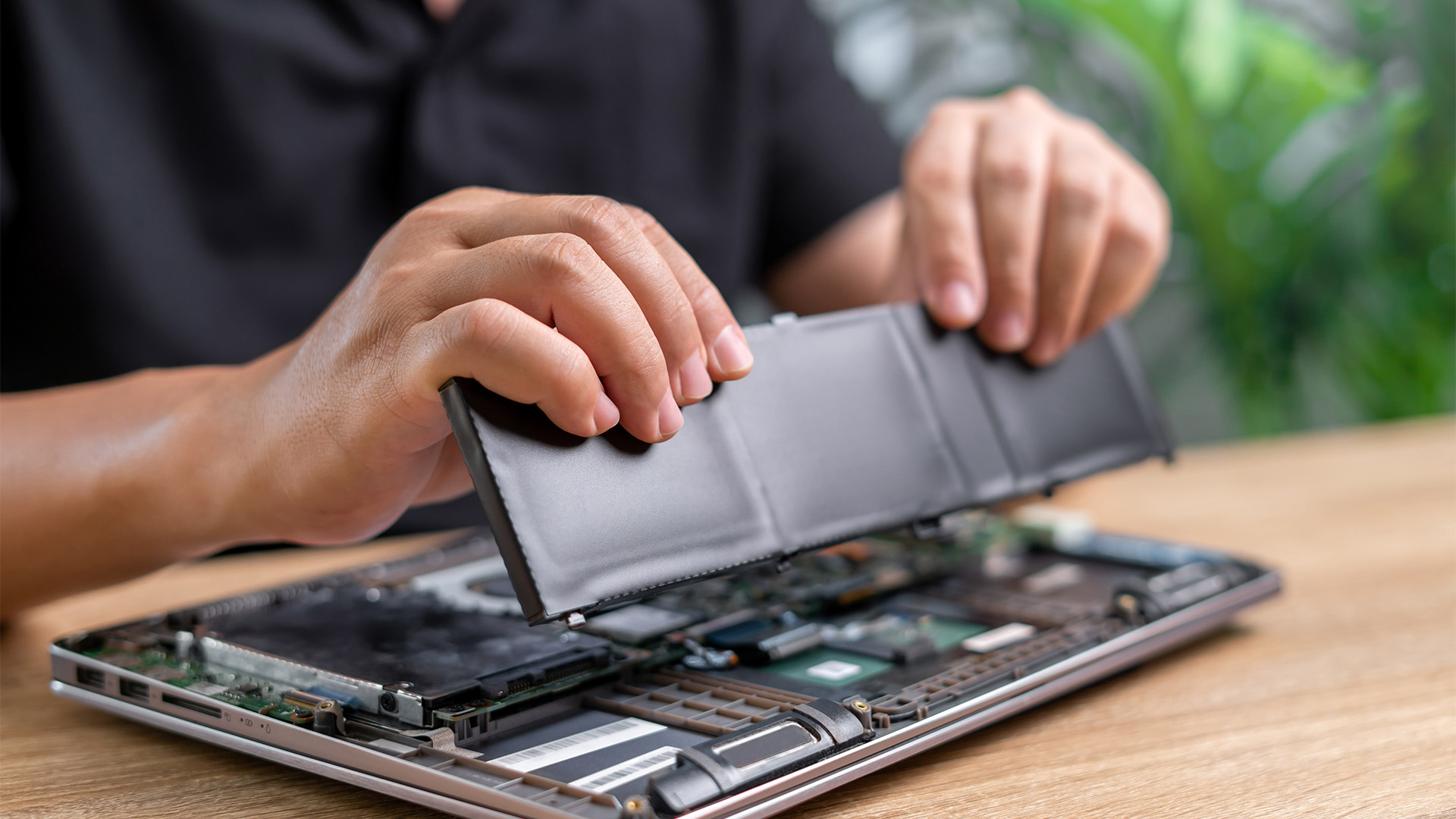 A technician carefully holding and replacing an internal laptop battery on a workbench.