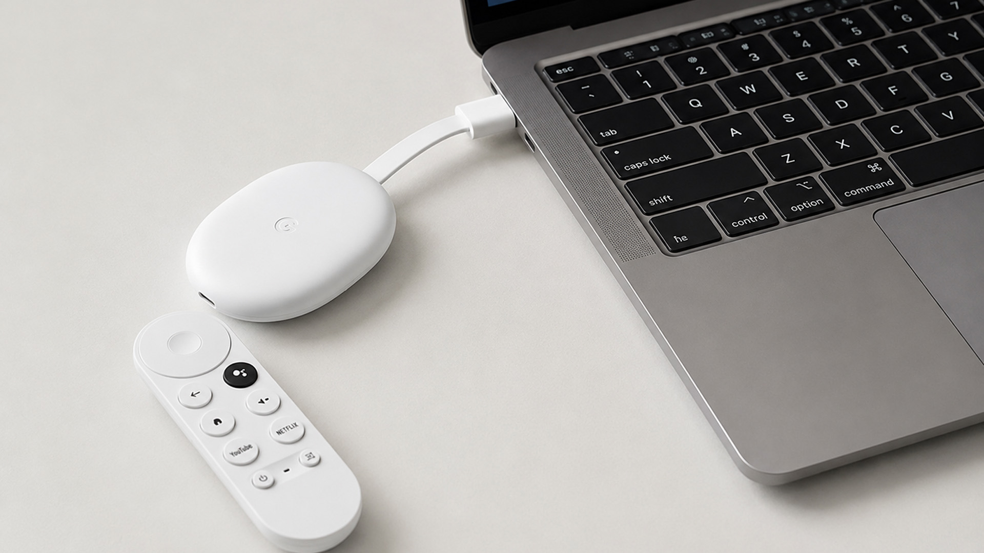 White Chromecast with Google TV and remote next to an open laptop.