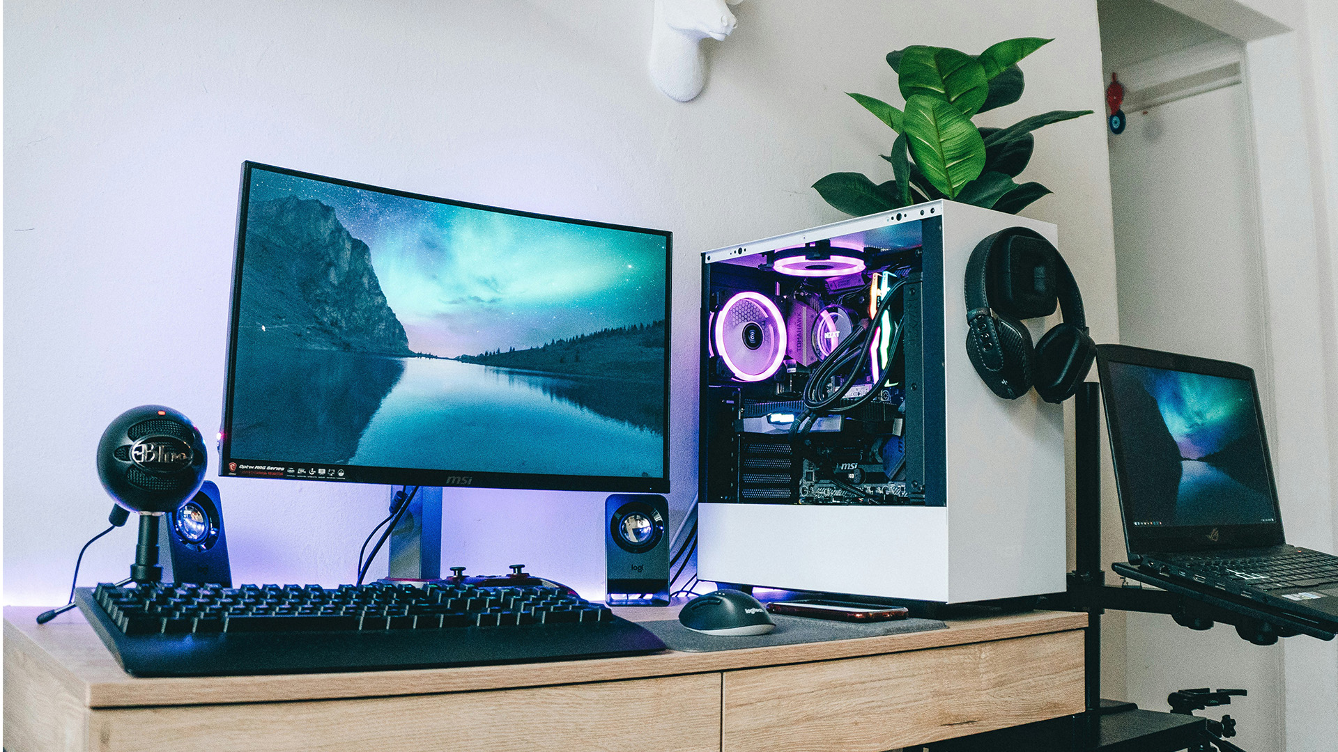 A white gaming PC tower and monitor set up with RGB lighting on a wooden desk.