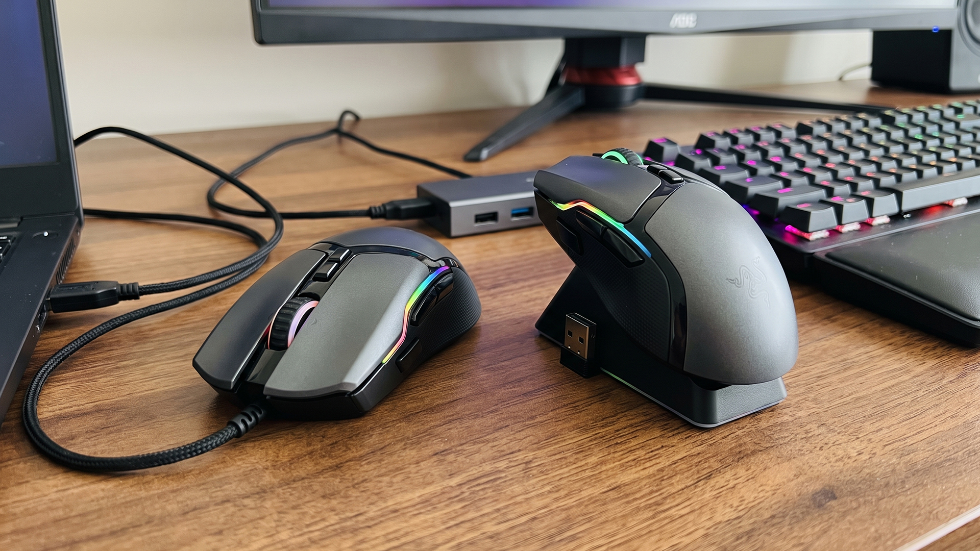Side-by-side comparison of a wired and wireless RGB gaming mouse on a desk.