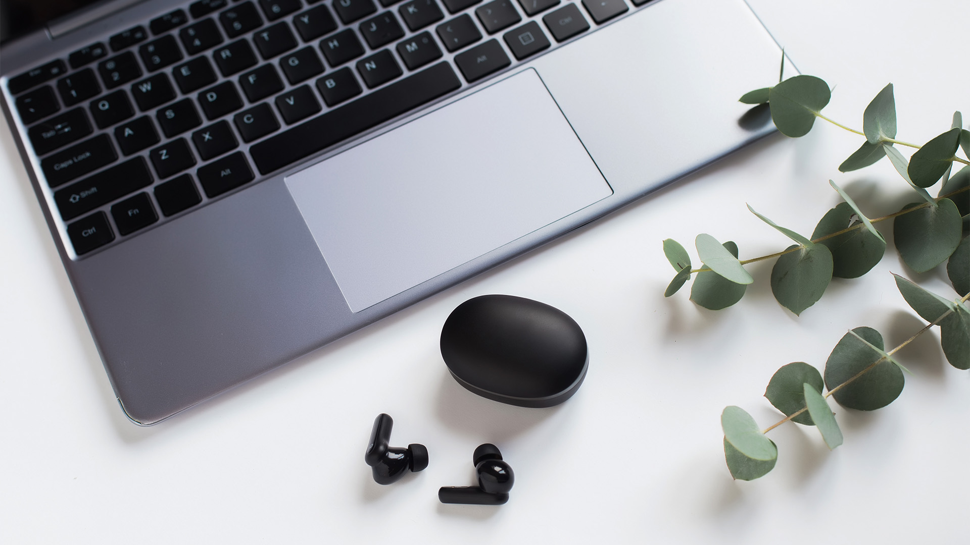 Black wireless earbuds and their charging case placed beside a laptop keyboard.