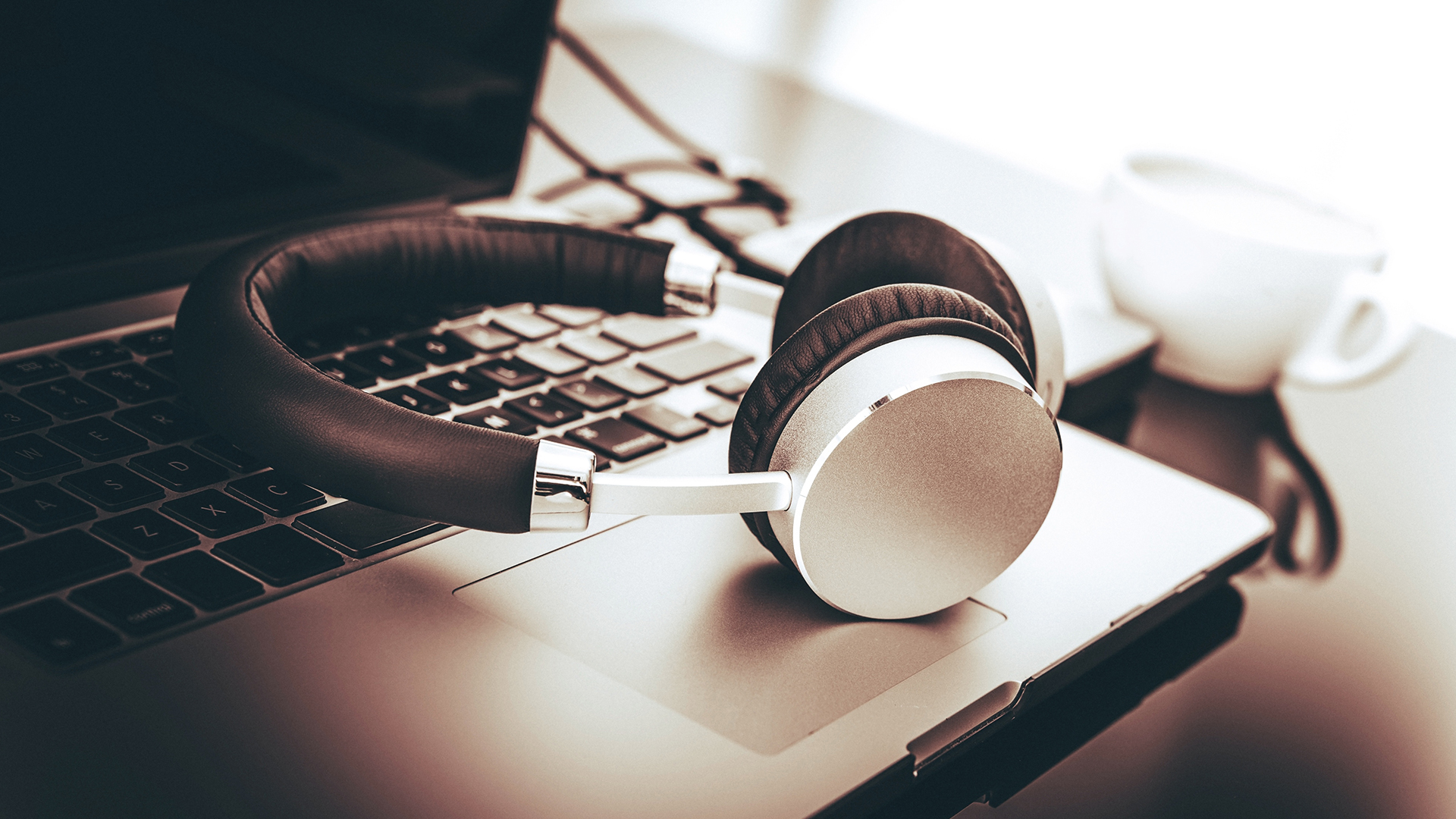 Silver wireless headphones resting on a laptop keyboard on a desk.