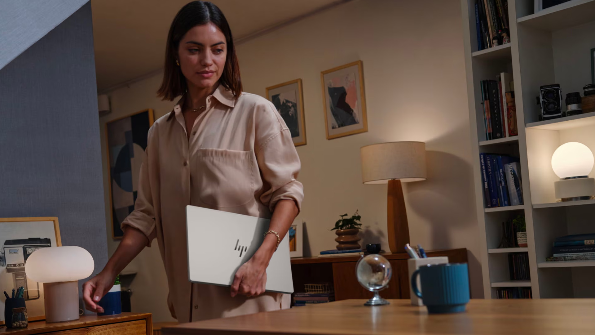 A woman holding a sleek HP laptop under her arm in a living room.