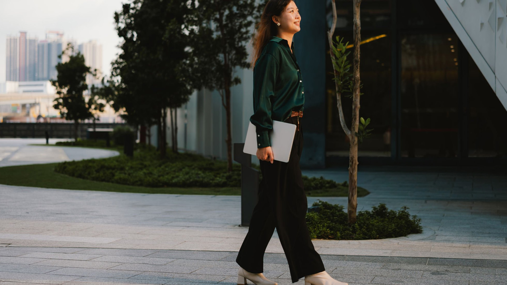 oman walking outside carrying a closed laptop under her arm.