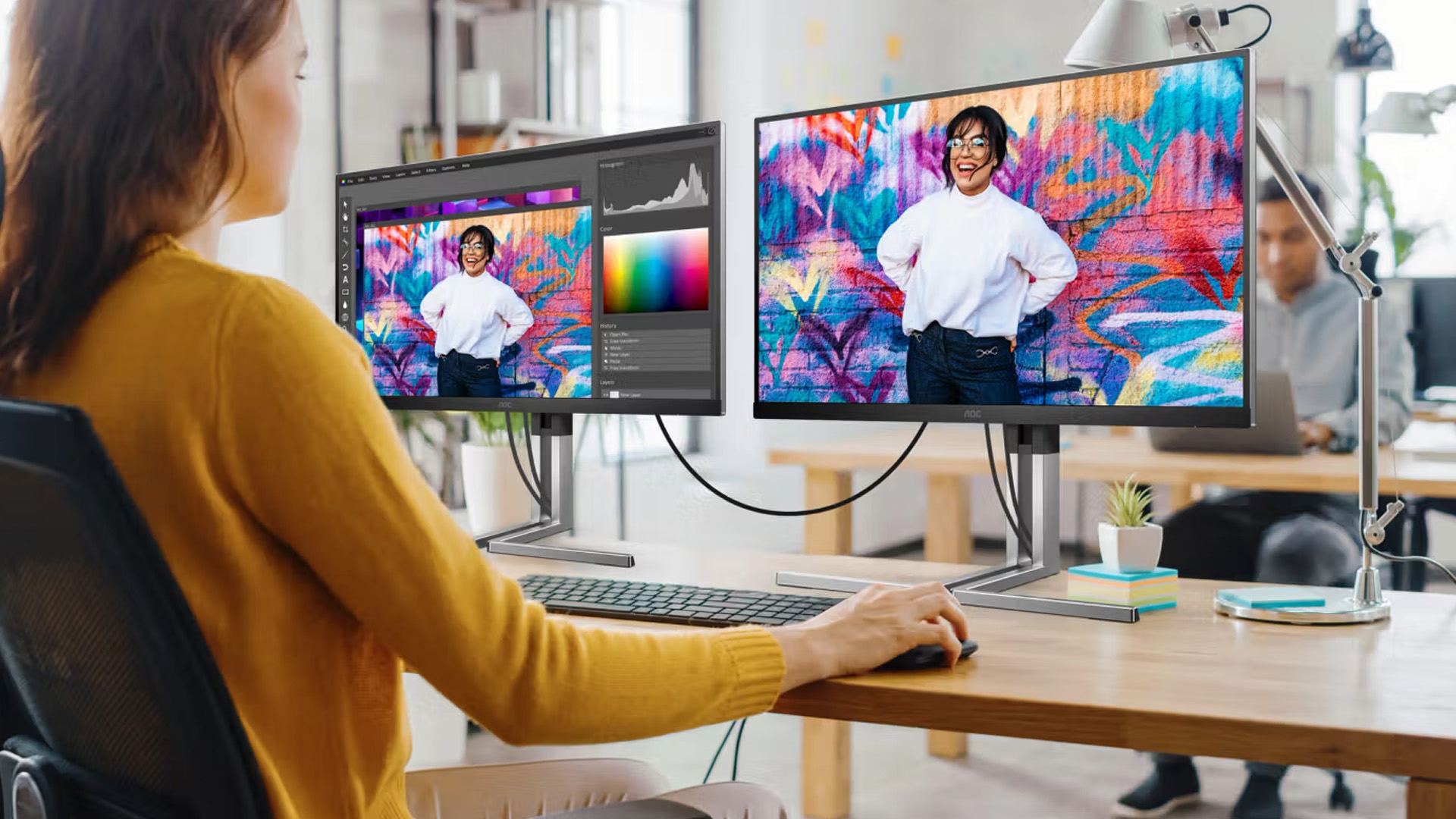 Woman editing a vibrant portrait photo on dual AOC monitors at an office desk.