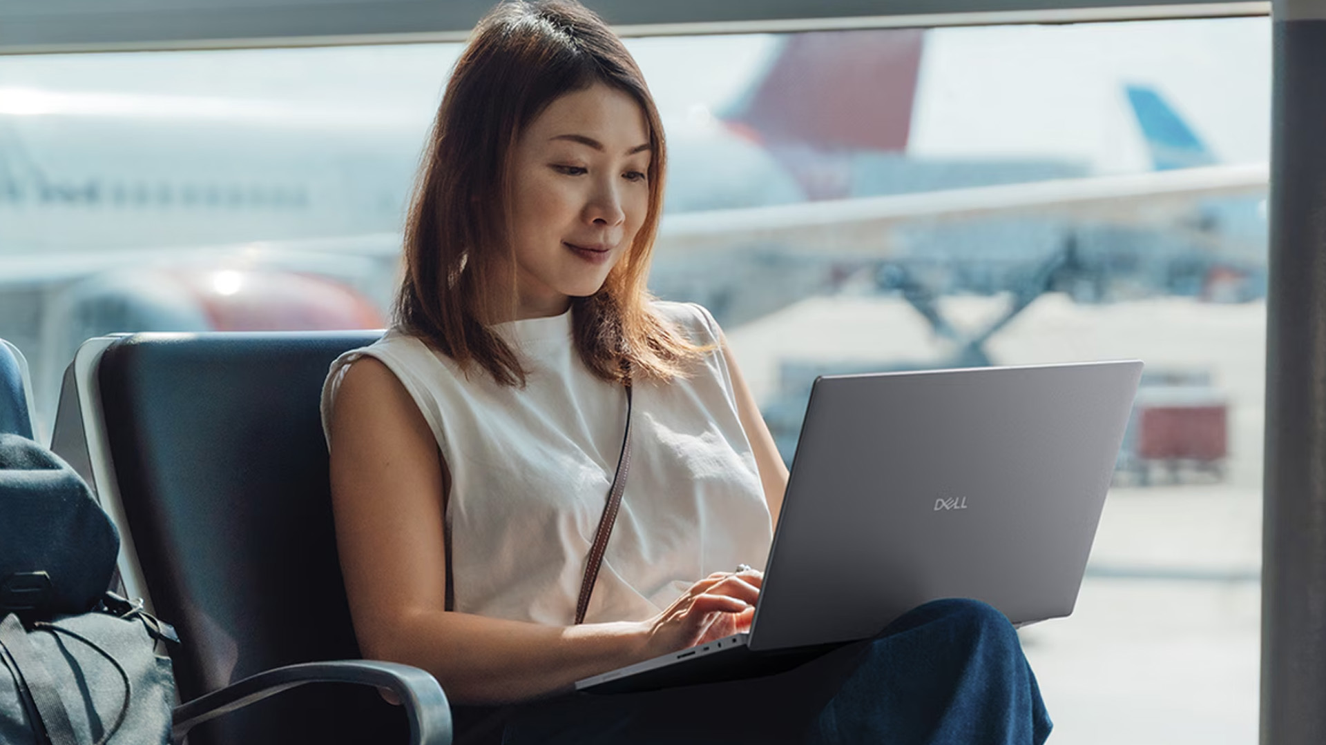 Woman typing on a portable Dell laptop while sitting in an airport lounge.