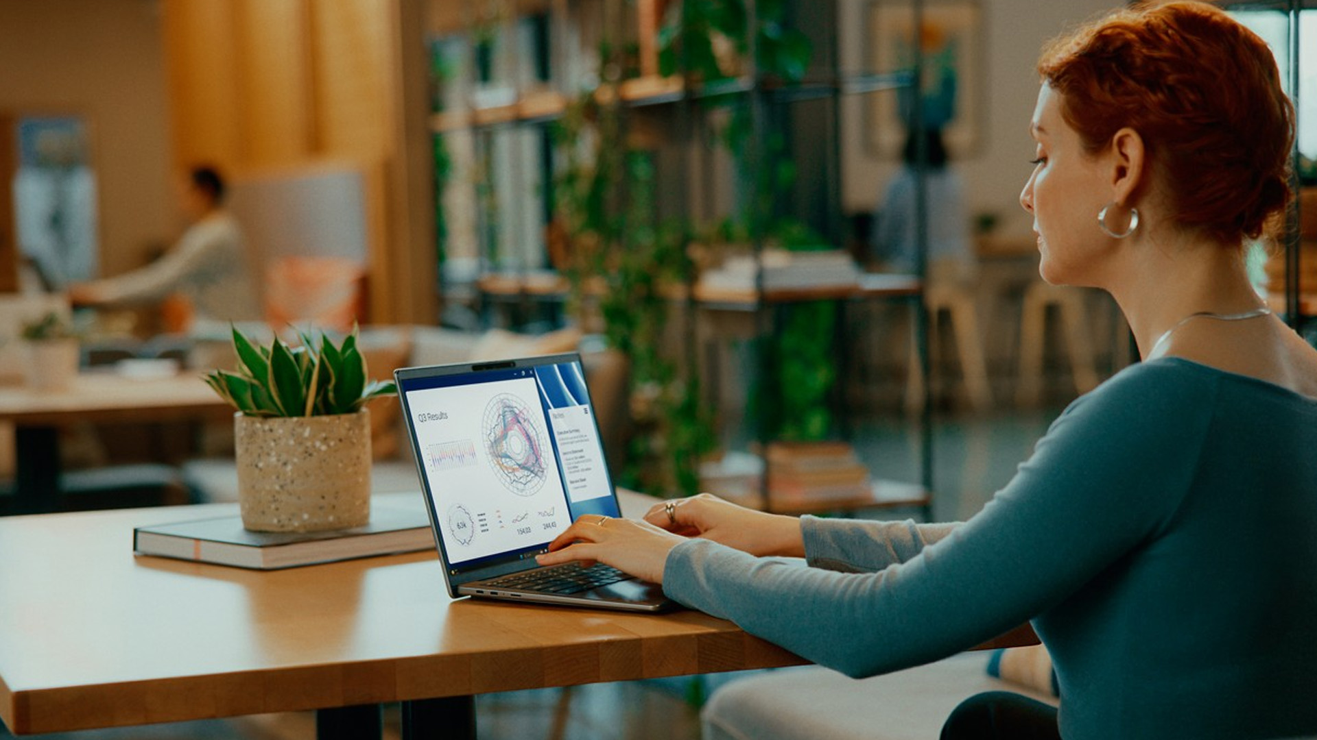 Woman typing on a Dell laptop showing data charts in a modern cafe.