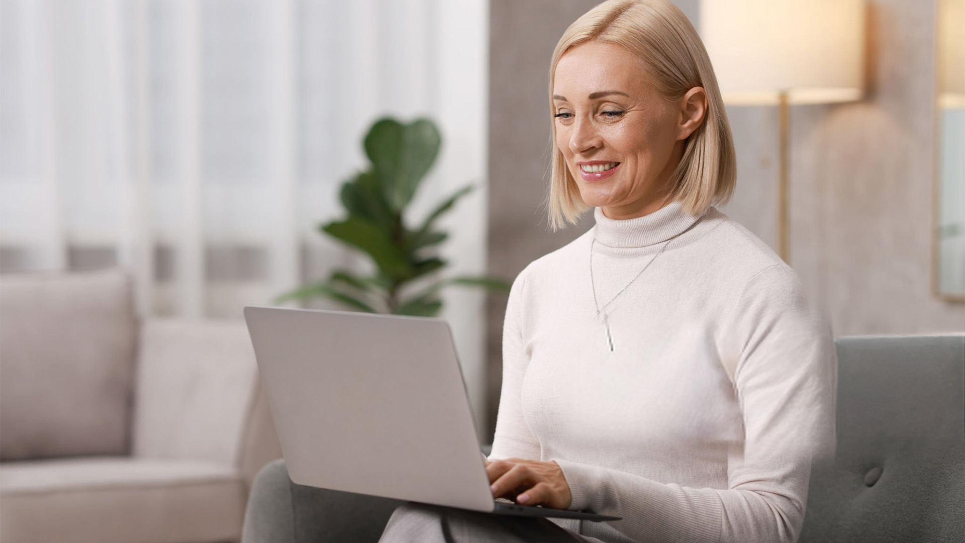 Woman in a white sweater using a laptop while sitting on a couch.