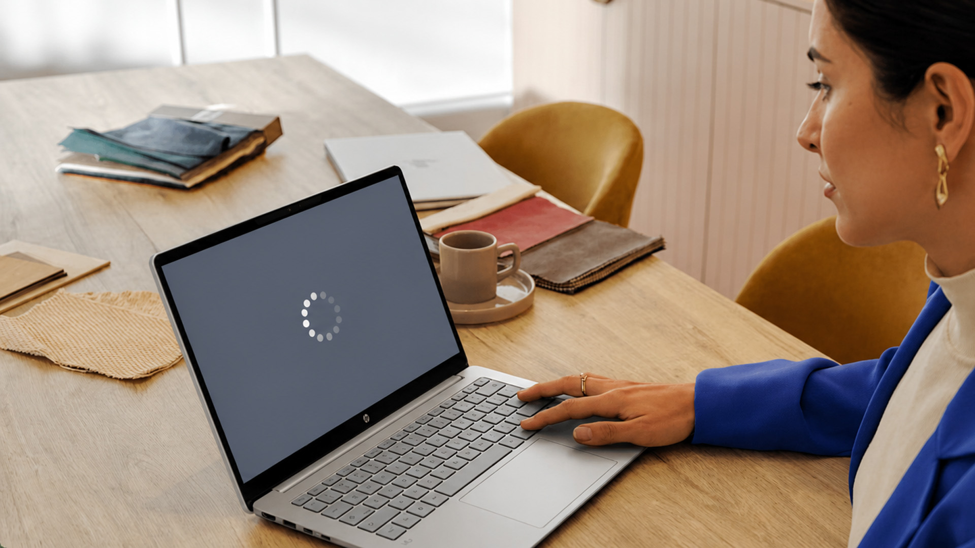 A woman sitting at a wooden desk while looking at a loading screen on her HP Chromebook.