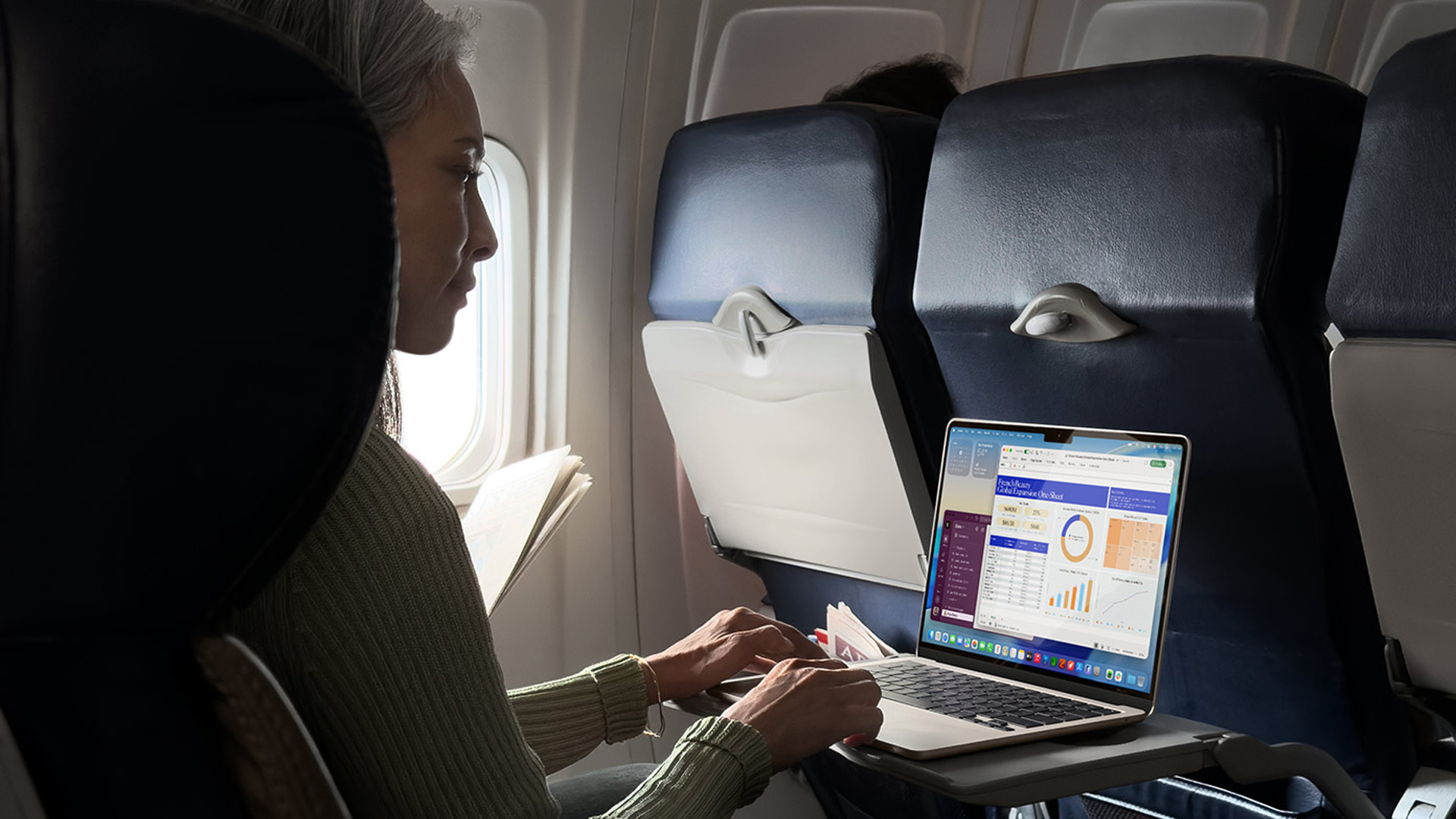 Woman working on a MacBook Air laptop on an airplane tray table.