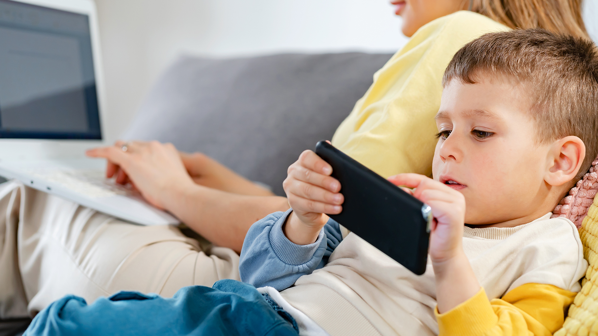 A young boy holding a smartphone while relaxing on the sofa at home.