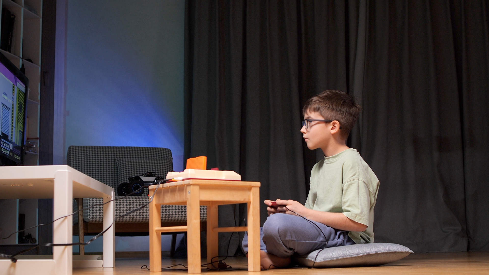Young boy sitting on the floor playing video games with a wired console controller.